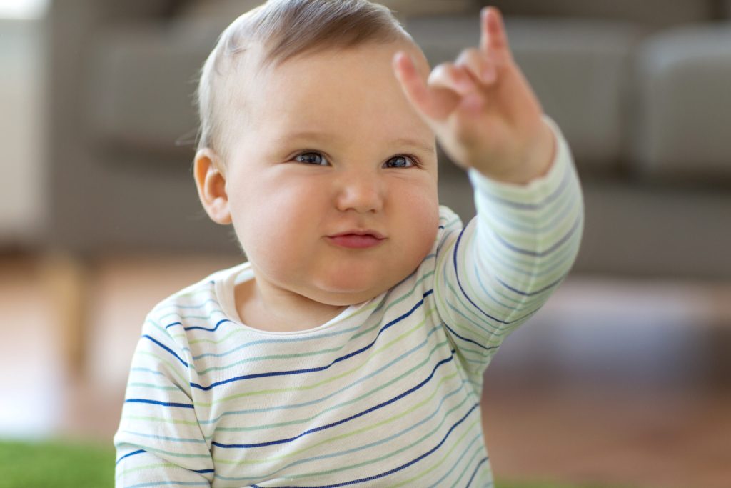 Bébé assis faisant un signe avec la main