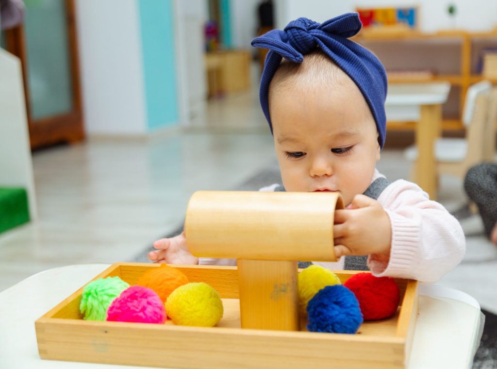 Bébé fille avec un nœud sur la tête jouant avec un jeu en bois et des pompons multicolores de type Montessori